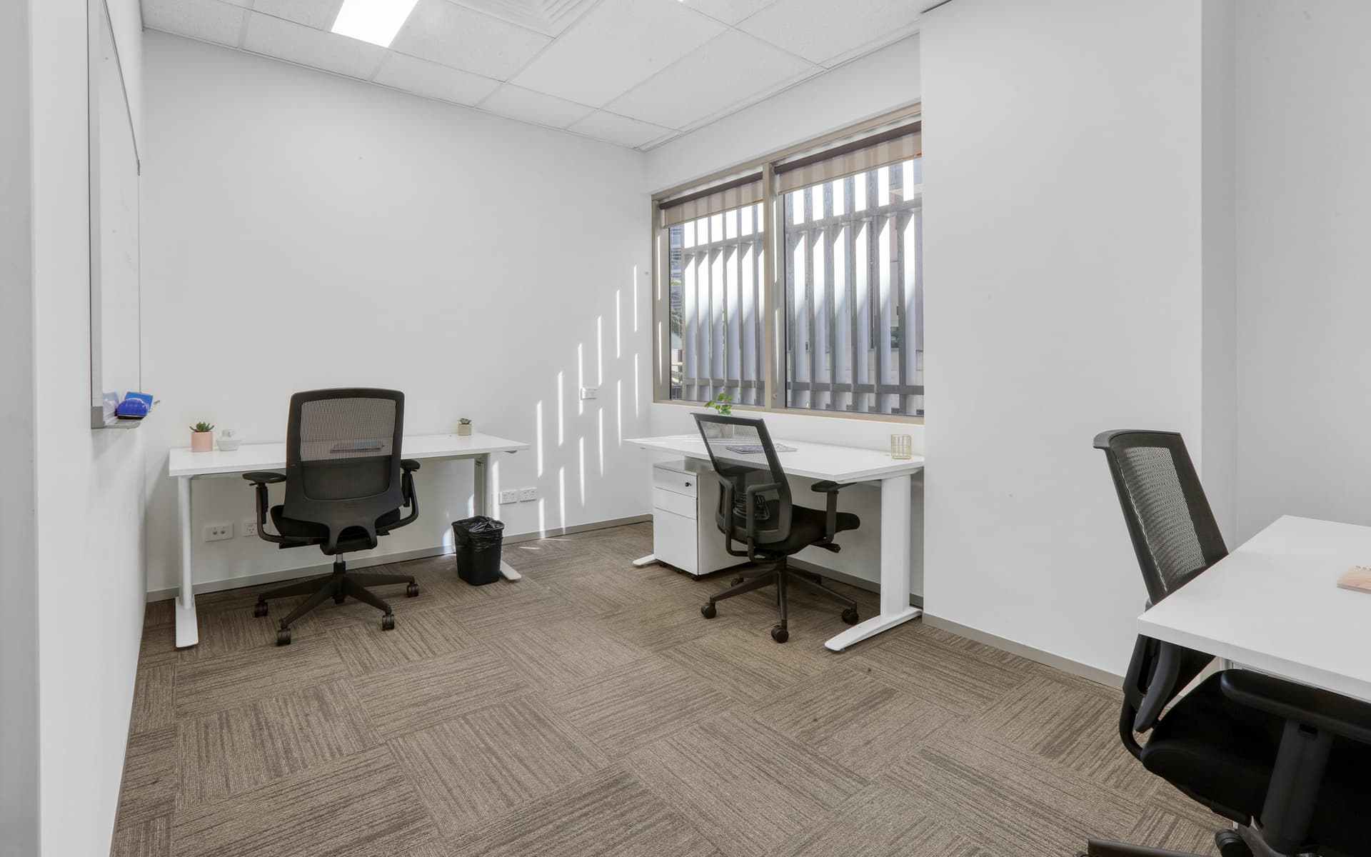 Small office space with white desks, black chairs, and window.