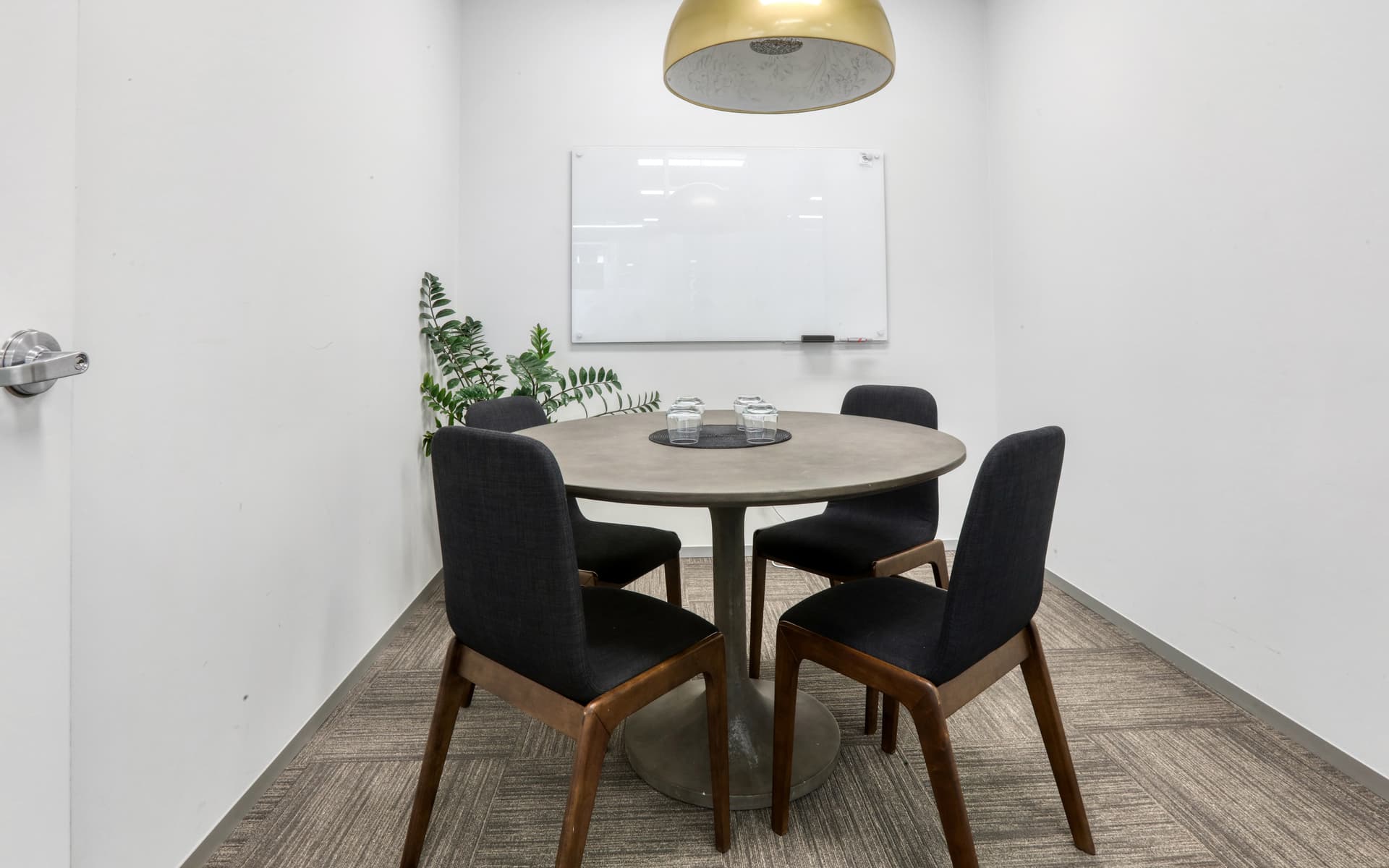Small meeting room with round table, four chairs, and whiteboard. Modern, minimalist office space.