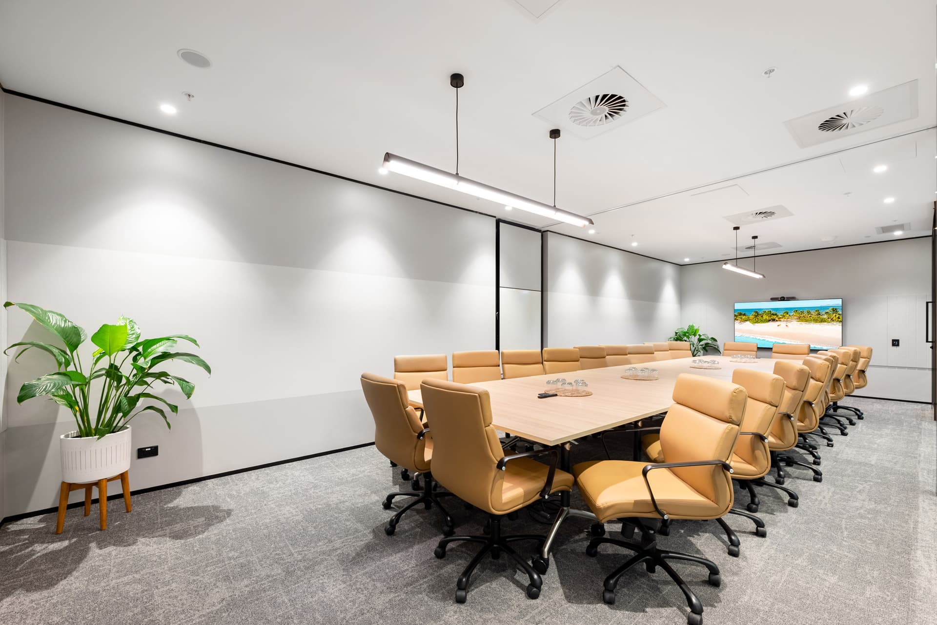 Bright modern conference room with a large table, tan leather chairs, and beach scene on a wall-mounted TV.