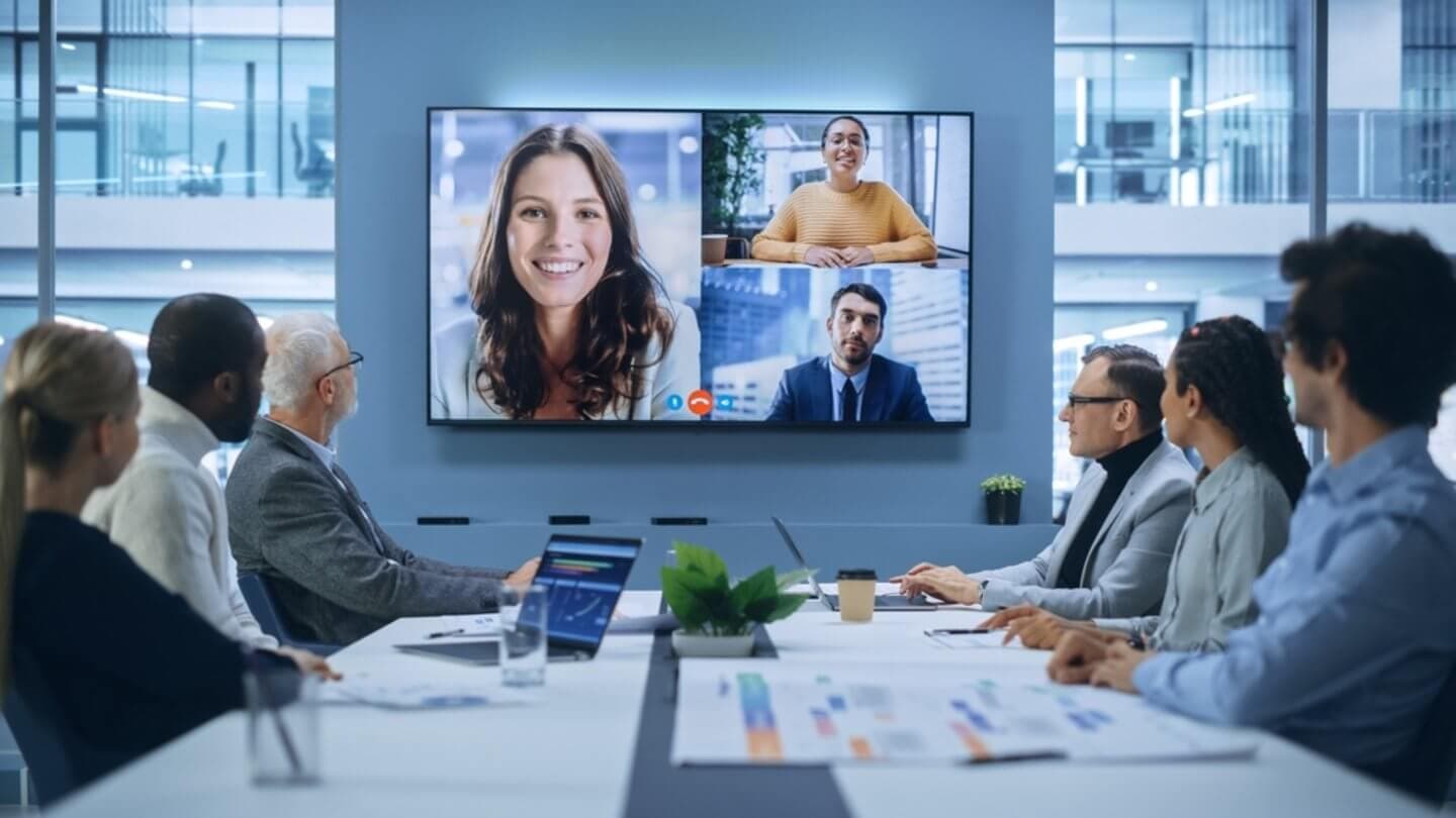 A business meeting in a modern meeting room, featuring a video call between colleagues