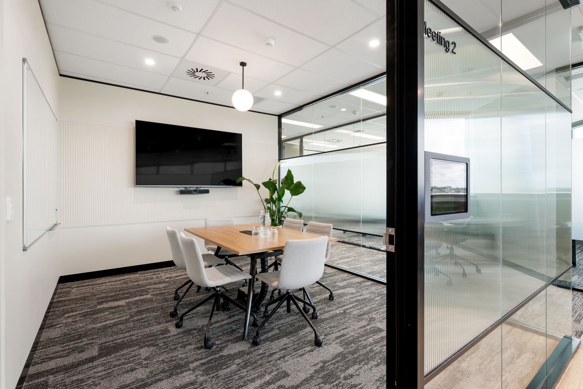 Modern meeting room with table, chairs, and large screen. Glass-walled meeting room