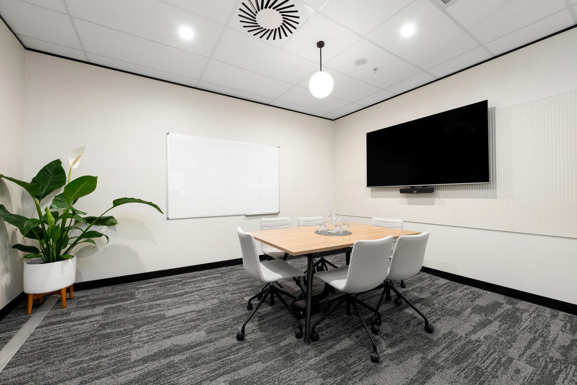 Small conference room with a dark wood table, grey chairs, whiteboard, and large screen on the wall.