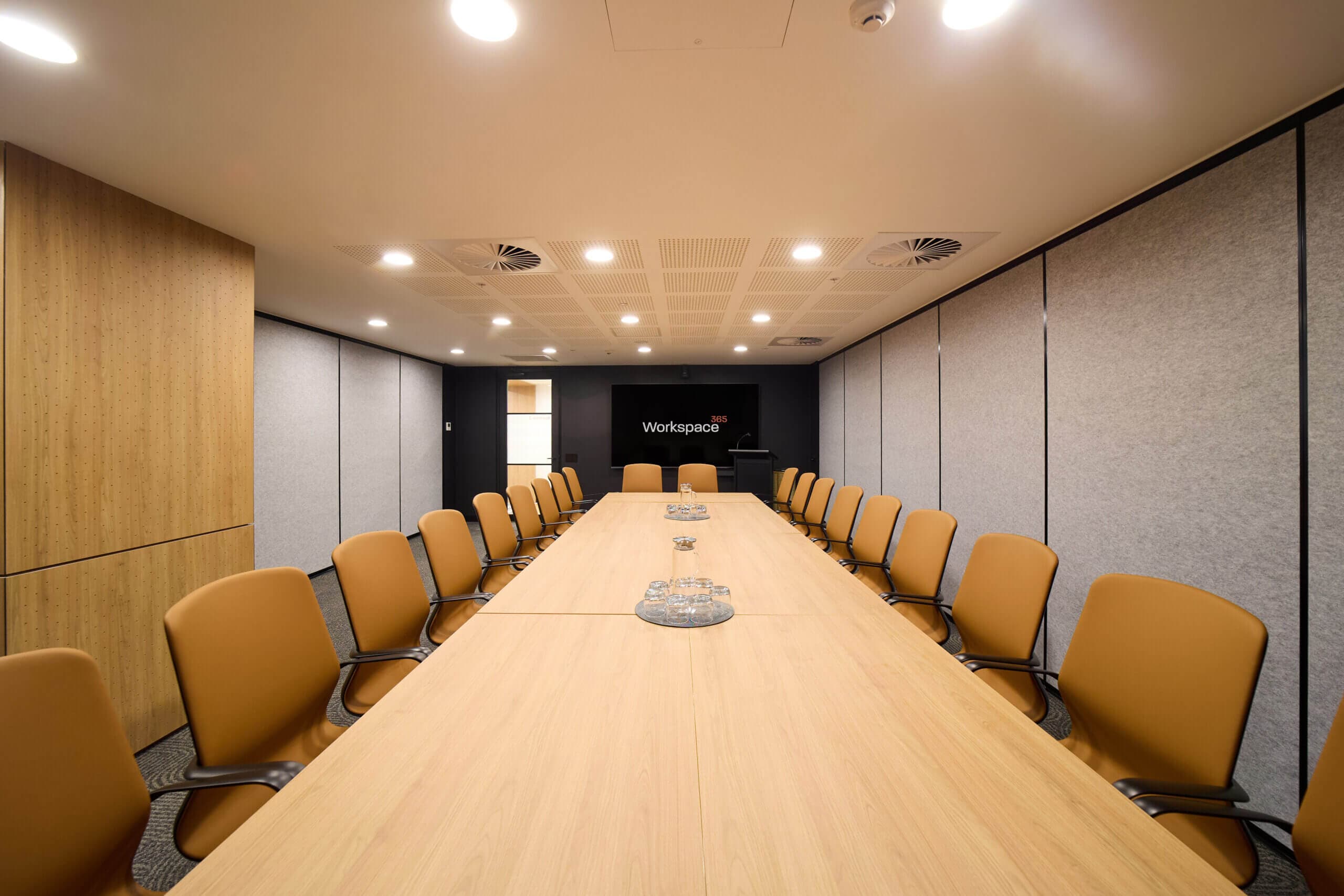 Modern conference room with long table, tan chairs, and Workspace logo on screen.