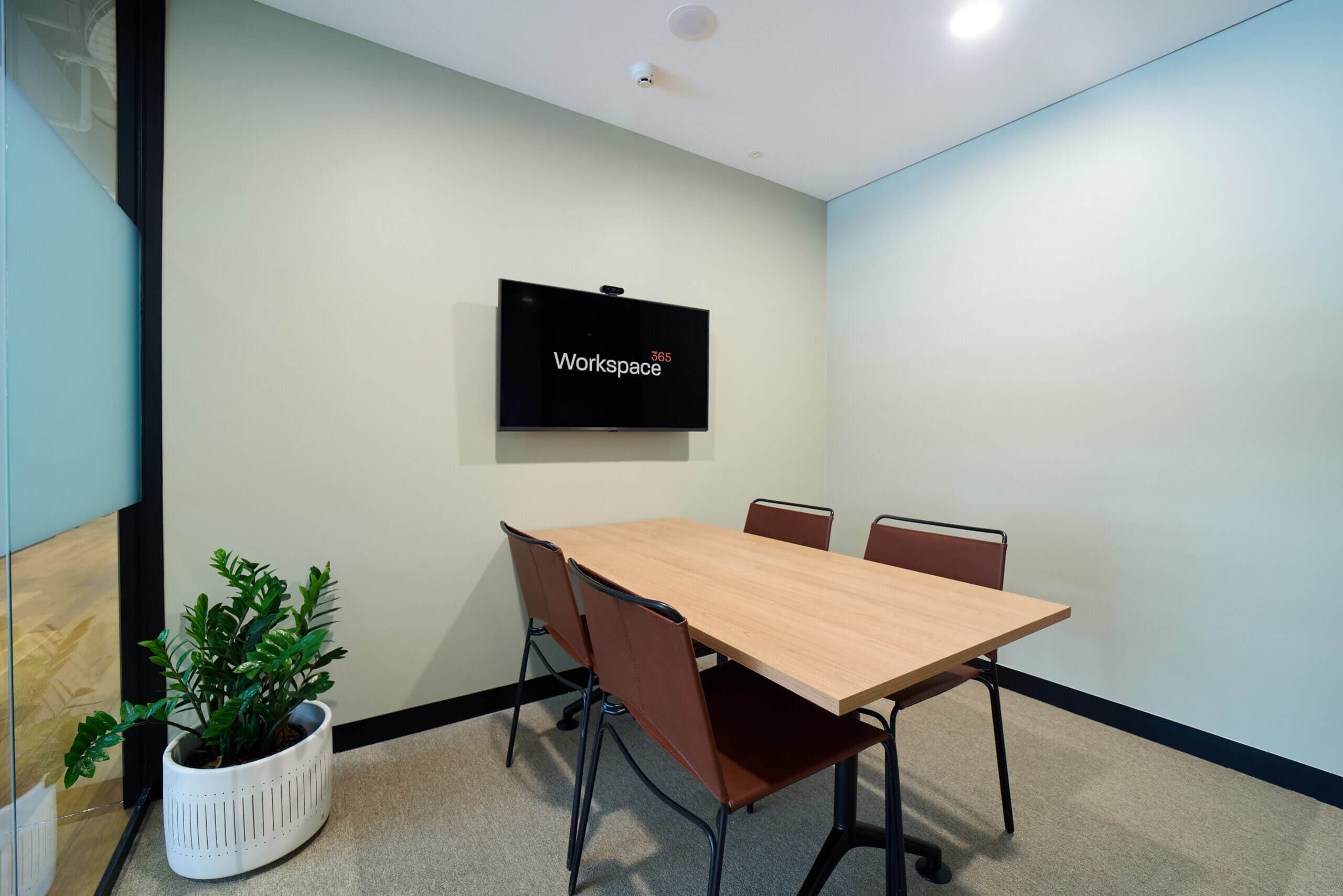 Small meeting room with table, four chairs, and a wall-mounted TV.