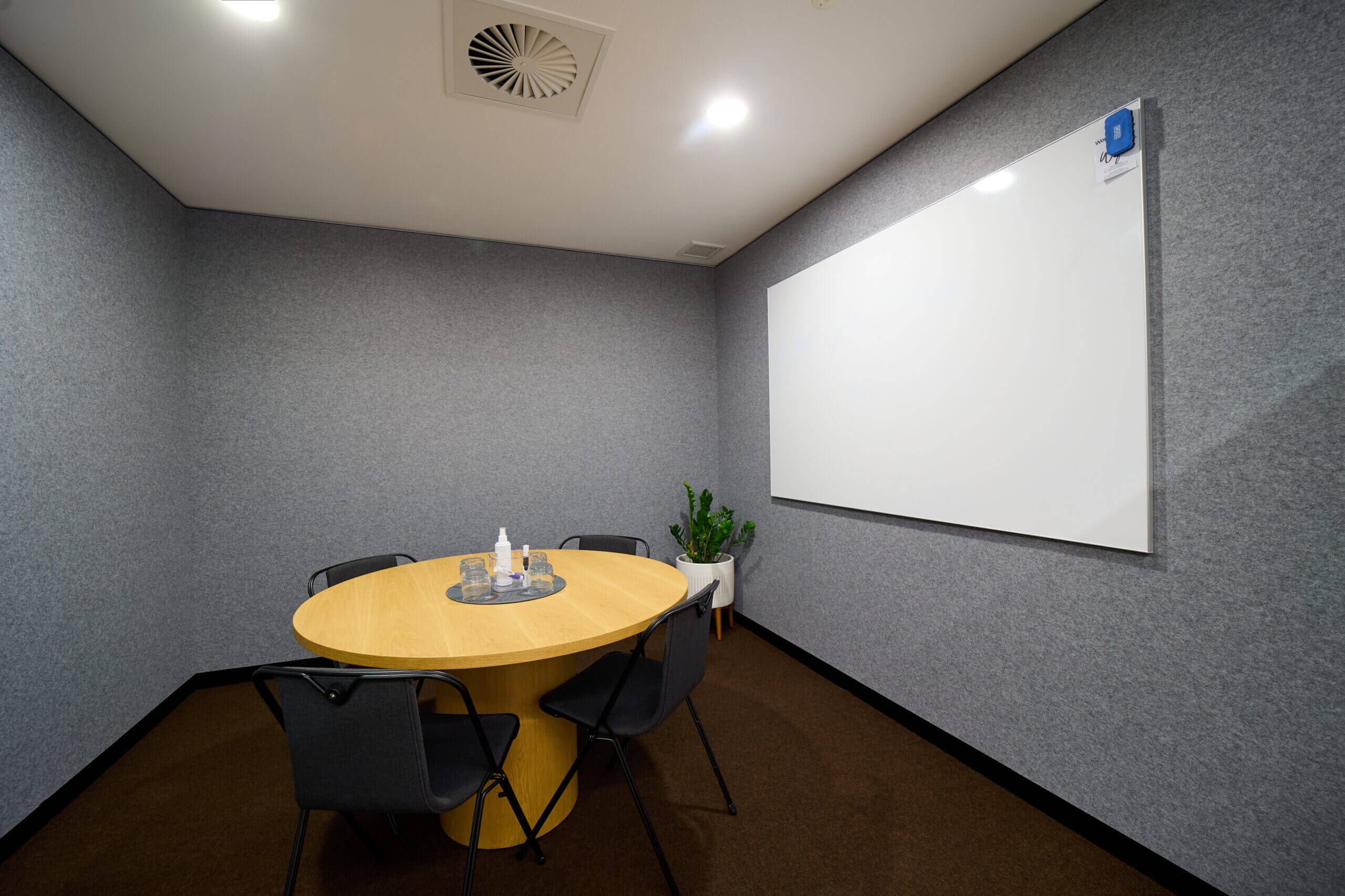 Small meeting room with table, chairs, whiteboard, and plant.