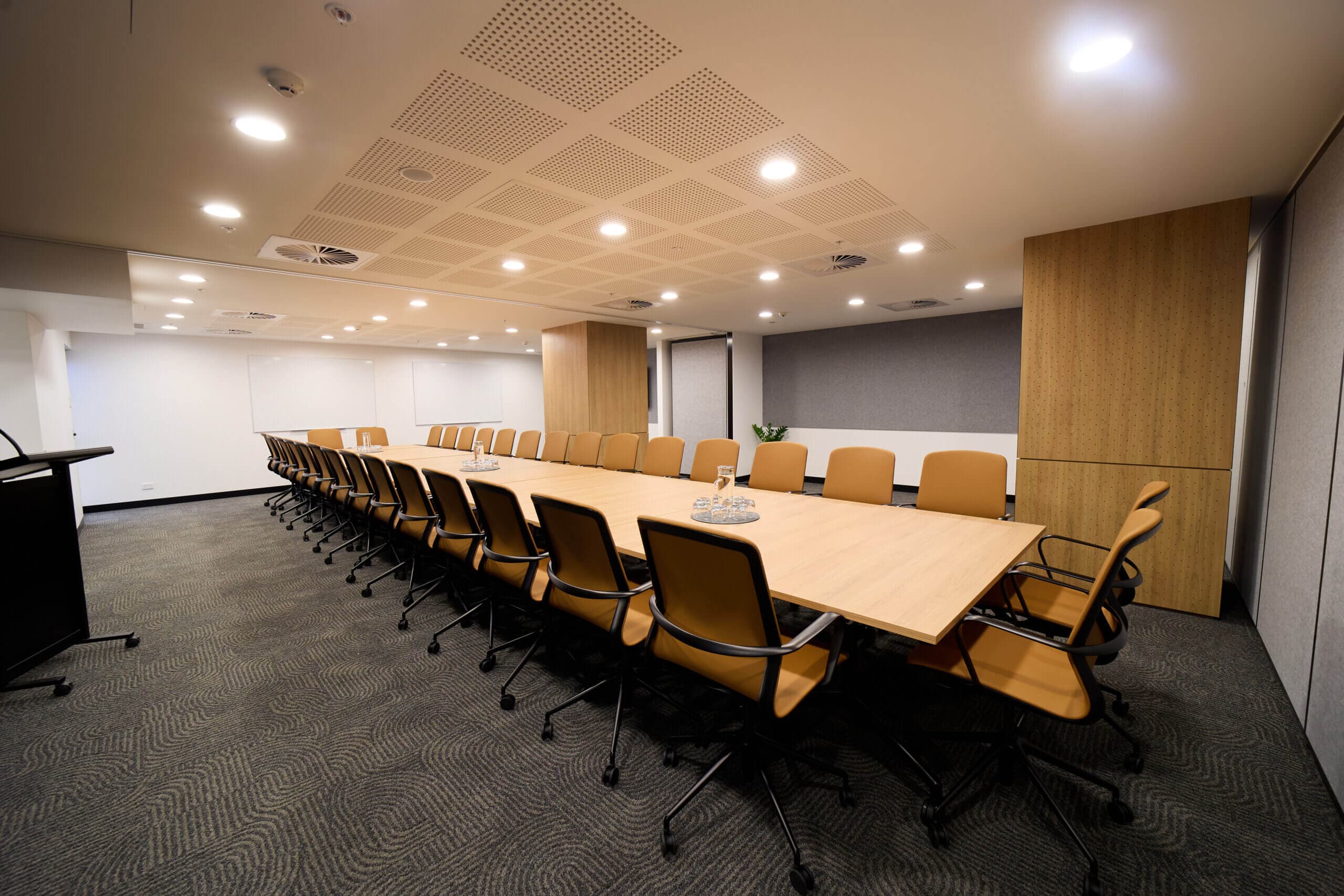 Conference room with long table, chairs, and presentation area. Bright lighting and modern design.