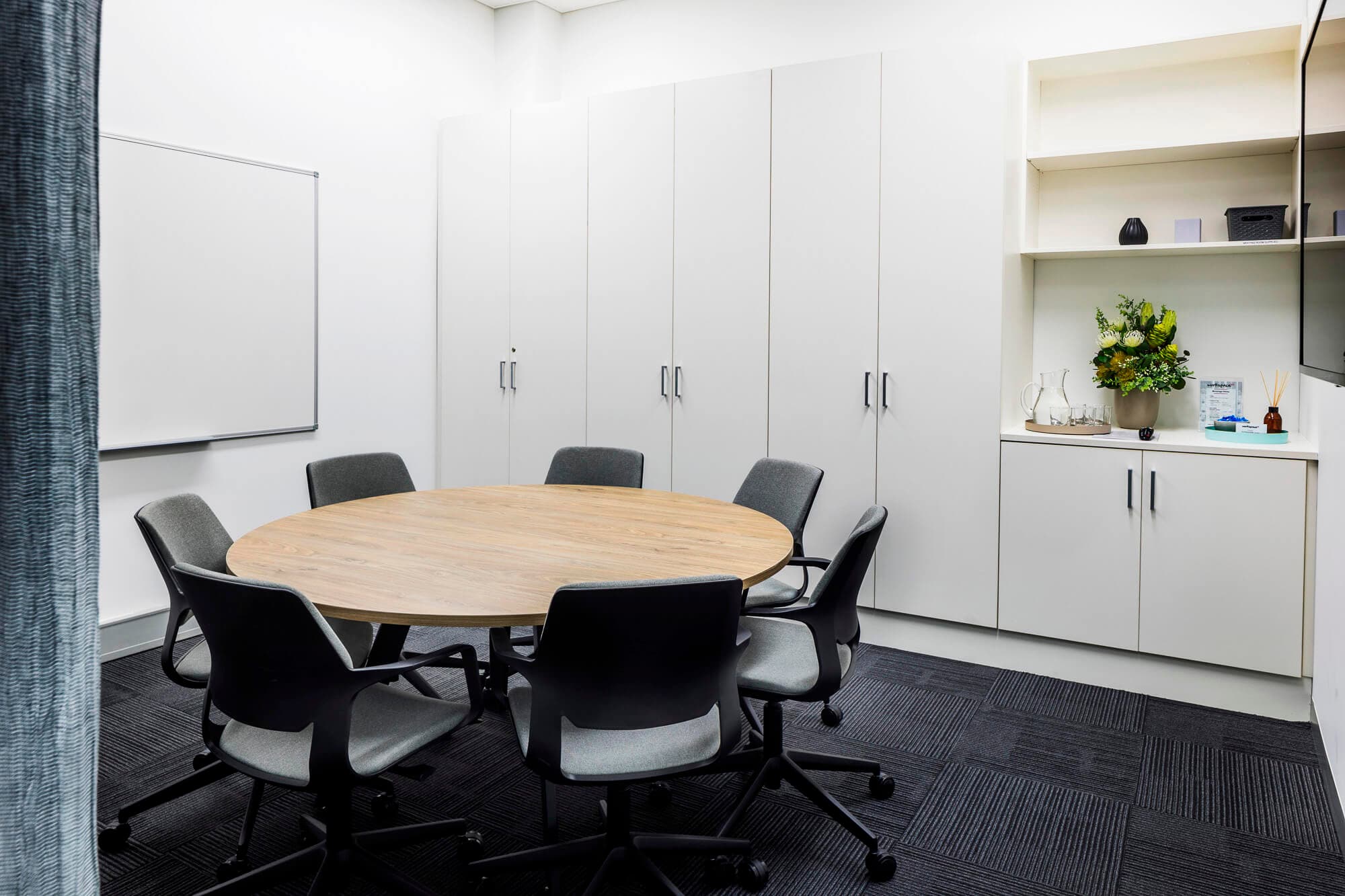 Meeting room with a round table, gray chairs, whiteboard, and built-in cabinets.