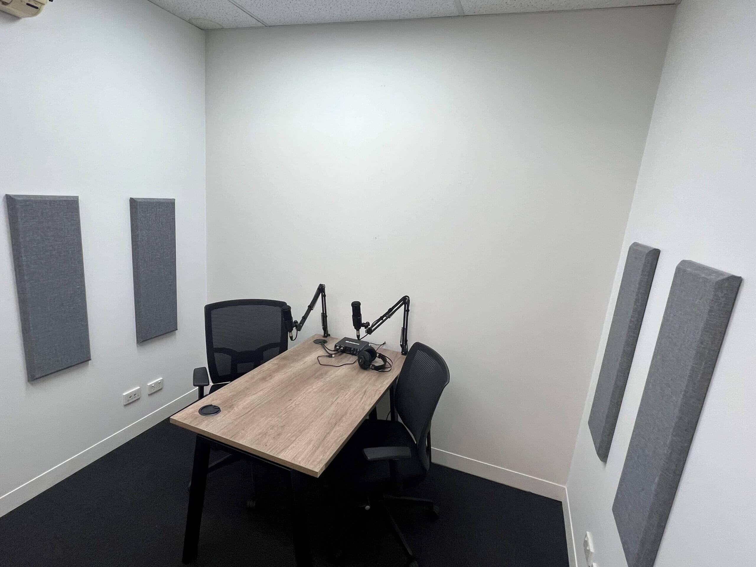 Podcast recording booth with two chairs, a table with a microphone, and soundproofing panels on the walls.