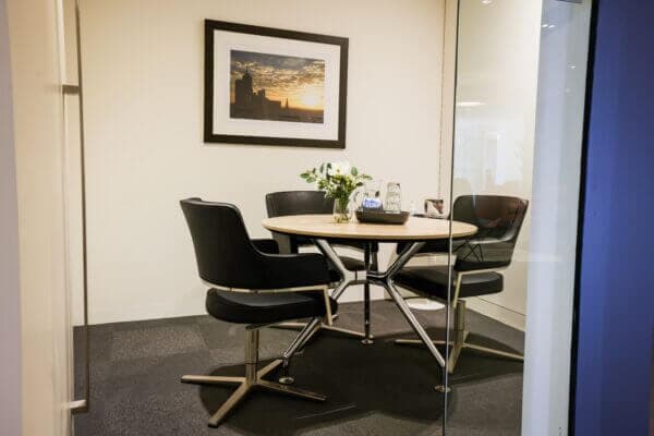 Small meeting room with table, comfortable chairs, artwork on the wall, and a glass partition.