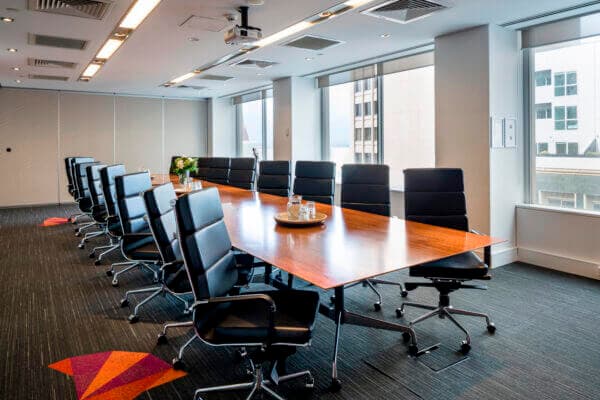 A modern conference room with a long wood table, black leather chairs, and large windows.